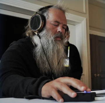 Rick Rubin leans over a small keyboard or control surface while wearing large open-back headphones, eyes closed in concentration. The source caption is ‘hey claude, clone discord,’ recasting a music-producer studio photo as a vibe-coding command.