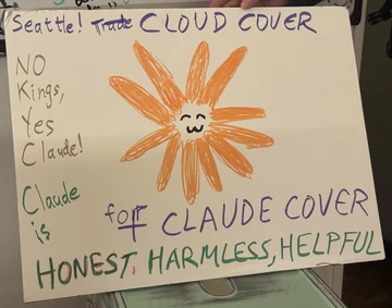 A handmade sign photographed at a Seattle “No Kings” protest features a hand-drawn orange Flower Claude. It reads, “Seattle! Trade CLOUD COVER,” “No Kings, Yes Claude!,” “Claude is for CLAUDE COVER,” and “HONEST, HARMLESS, HELPFUL.” The source poster says that a friend brought the sign to the protest.