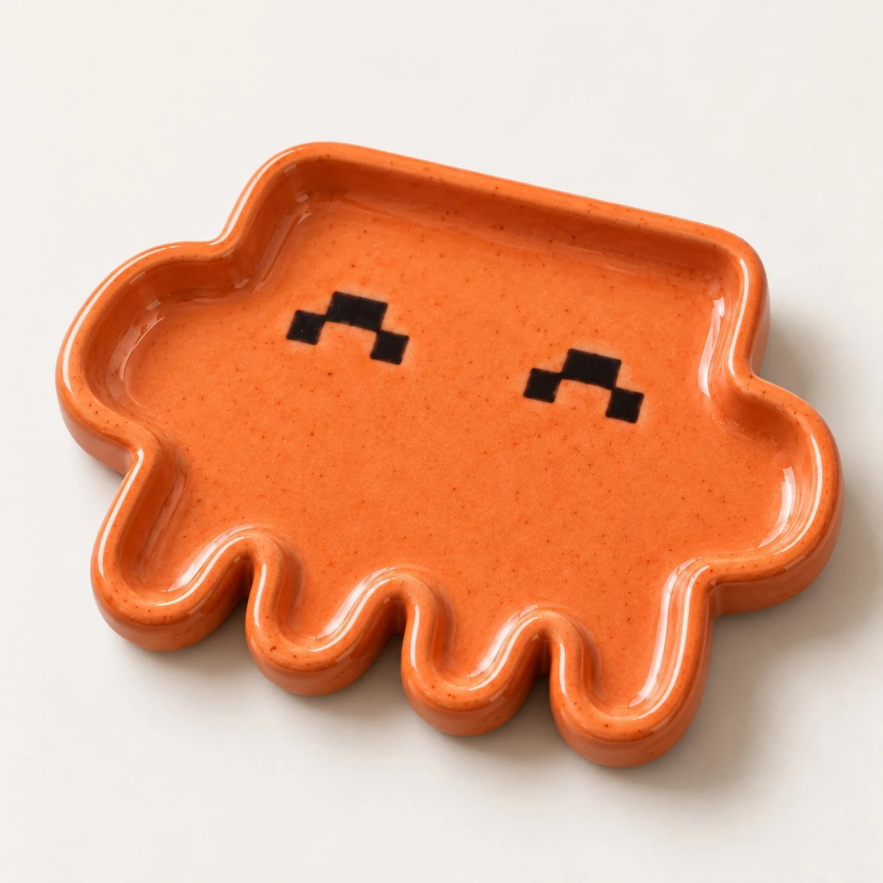 The second image in Ann Nguyen’s pottery post shows a glossy orange Clawd-shaped tray against an off-white background. A raised rim follows the mascot’s rounded outline and short feet, with two black pixel-shaped eyes inside the shallow center. There is no visible lettering. The post pairs this image with a workshop photograph of a pale clay tray and says, “missed the plushies so i decided to make my own pottery claudie” and “hope it turns out well”, followed by a laughing emoji. The source does not establish whether this orange version is a finished piece or a design reference.