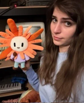 A woman holds an orange Claude plush toward the camera; the source asks an image model to animate her throwing it into the void.