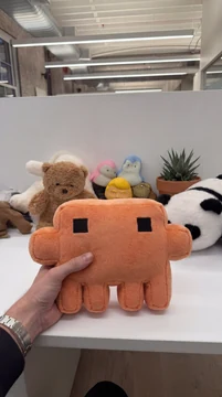 A person holds a handmade orange Claude plush in an office, with other stuffed toys in the background.