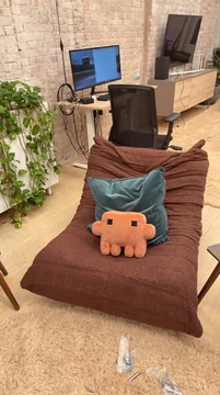 A handmade orange Claude plush sits upright in a chair in a modern office.