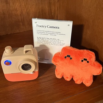 An official Claude plush poses beside a Poetry Camera exhibit at Code with Claude San Francisco.
