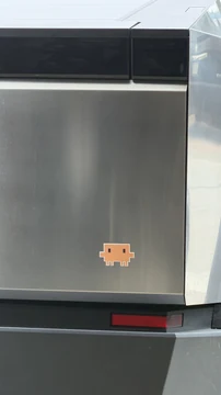 A small pixel Claude sticker is affixed to the stainless-steel door of a dishwasher.