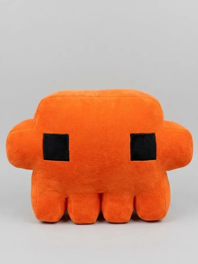 A product-style photograph of an orange Claude plush with square black eyes against a pale gray background.