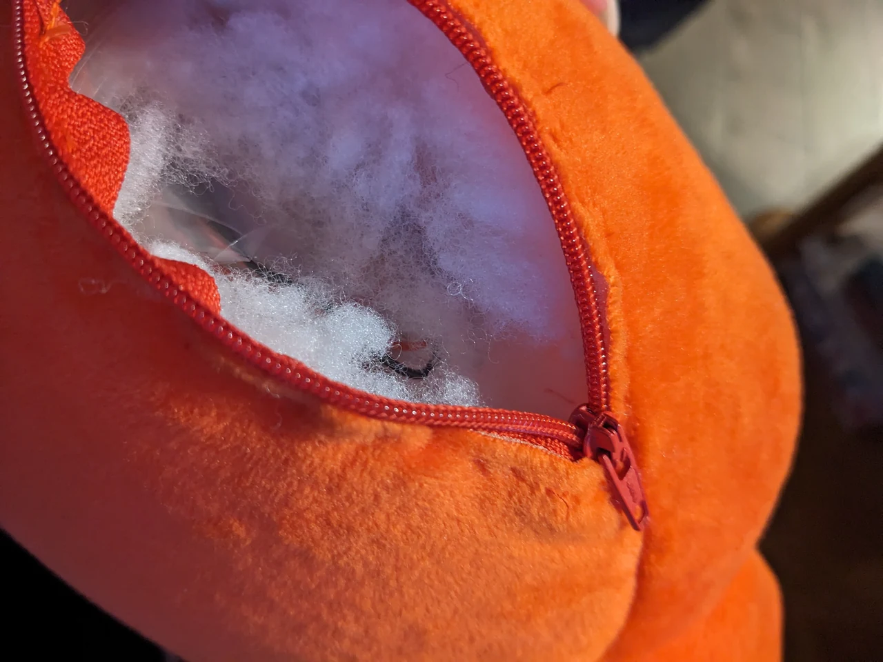 Close-up of the opened zipper on an orange Claude plush, showing the removable stuffing and internal pouch used for a hug sensor.
