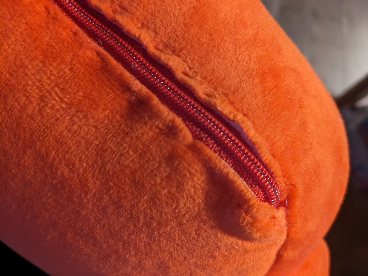 Close-up of the closed zipper installed along the back of an orange Claude plush for hug-sensor maintenance.